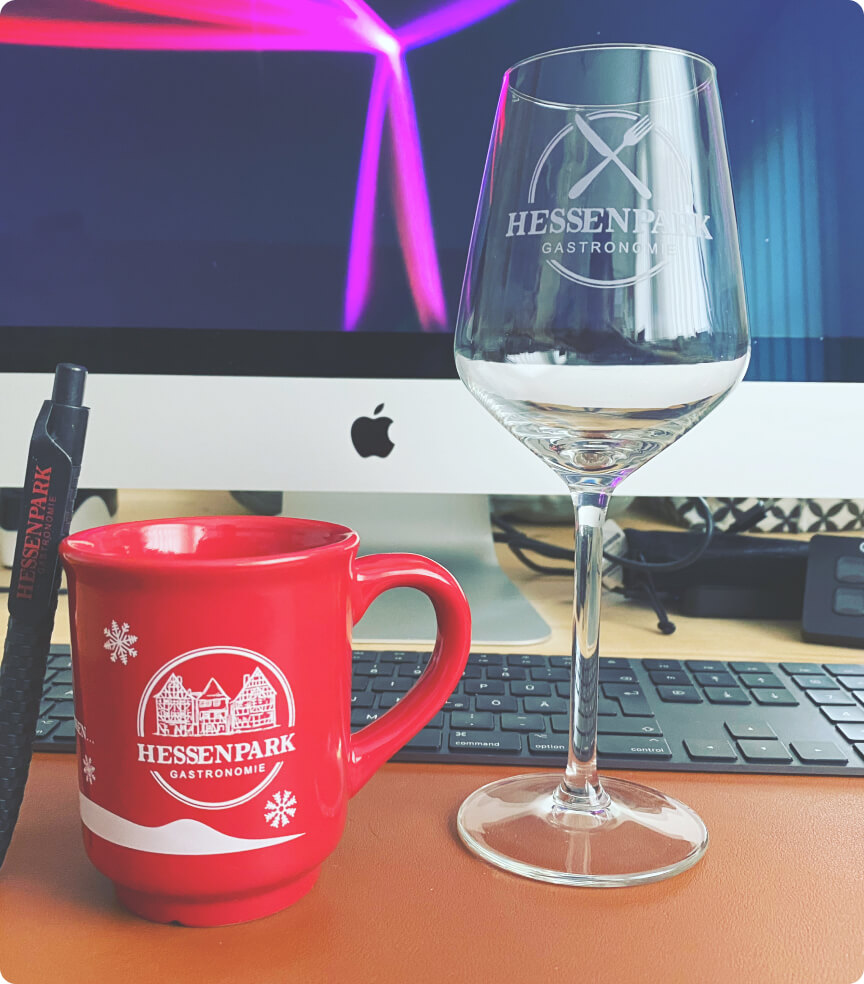 Ein Glas und eine weihnachtliche Tasse mit dem Logo von Hessenpark Gastronomie